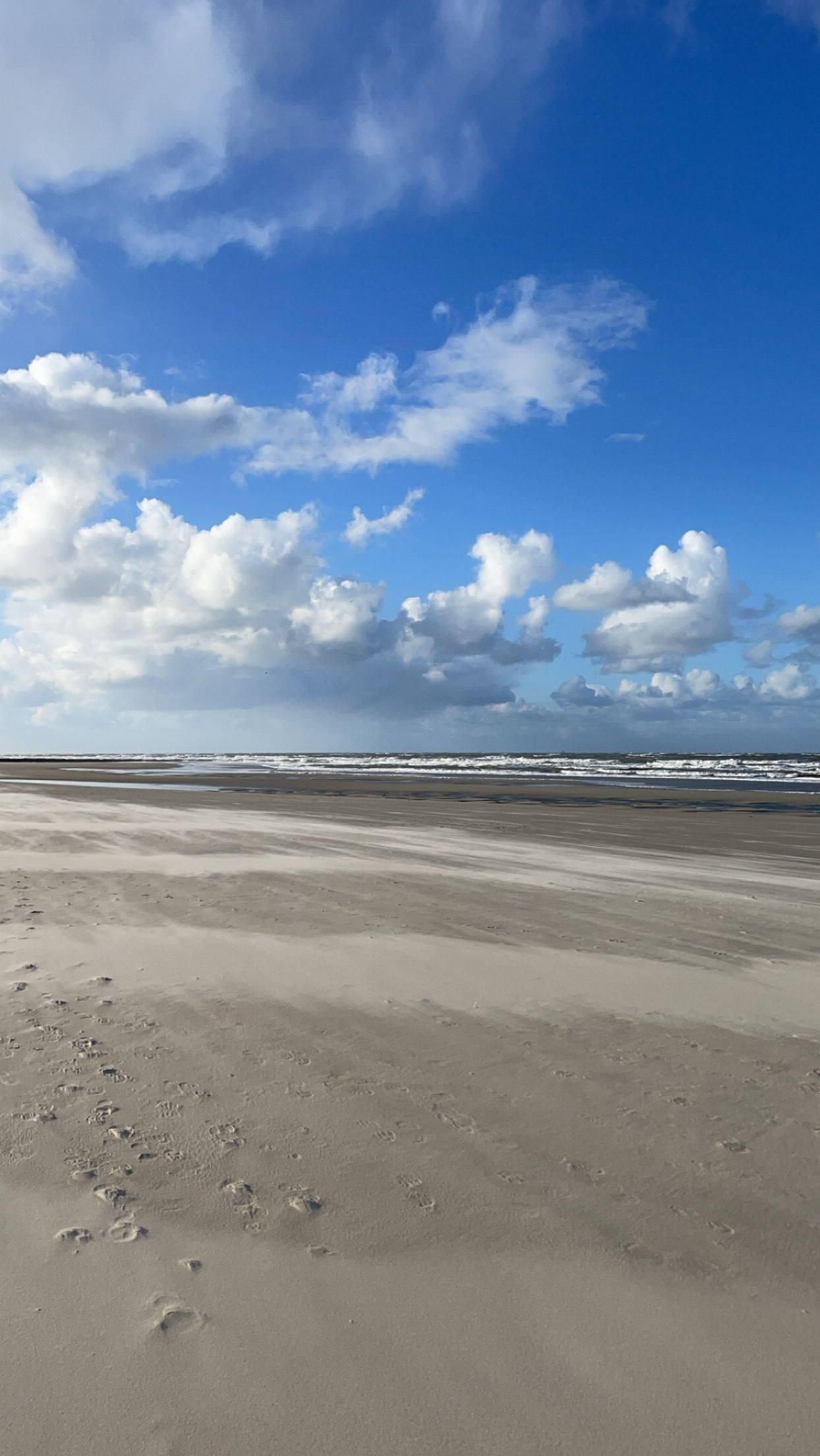 Vom Wind verwehter Sand am Strand, darüber dramatische Wolken