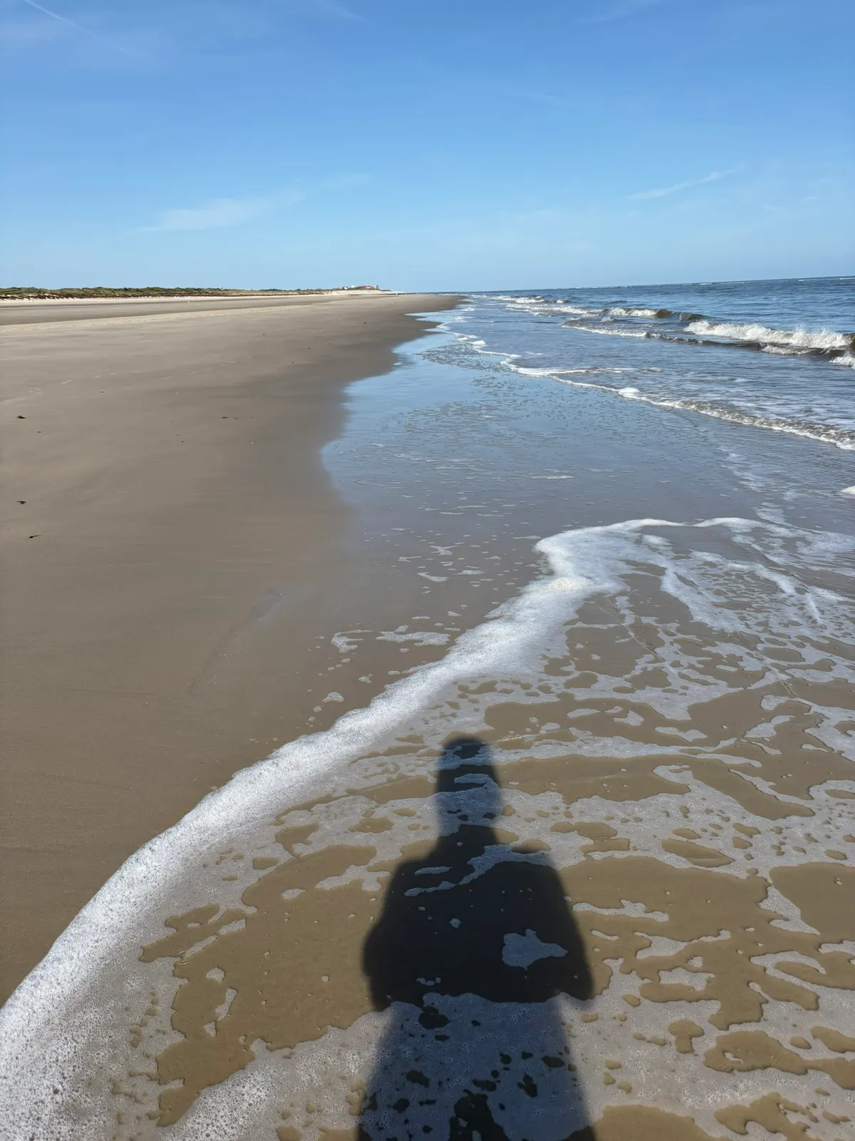 Schatten einer stehenden Person auf nassem Sand, berührt vom Meerschaum
