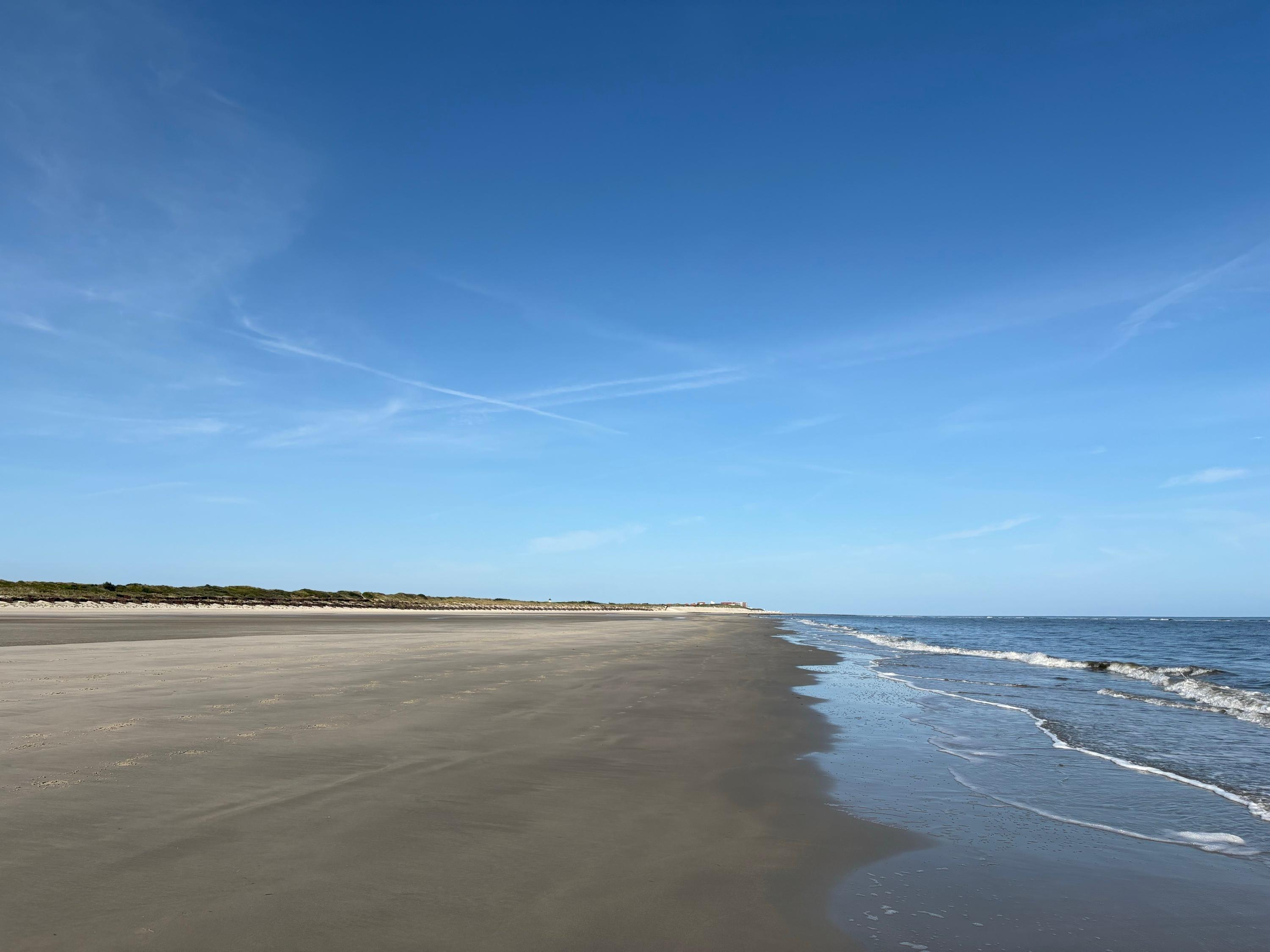Weiter, leerer Sandstrand auf Wangerooge unter hellem Himmel, rechts das ruhige Meer
